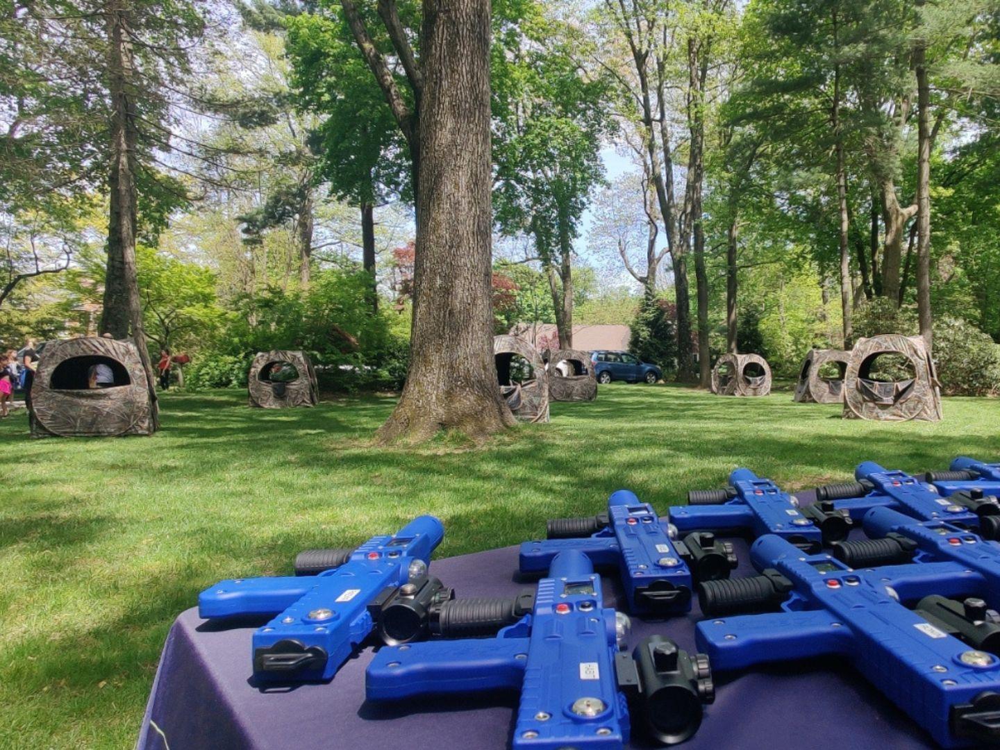 A backyard filled with camourflaged tents. a table wil blue laser taggers is on lower right side of the screen.